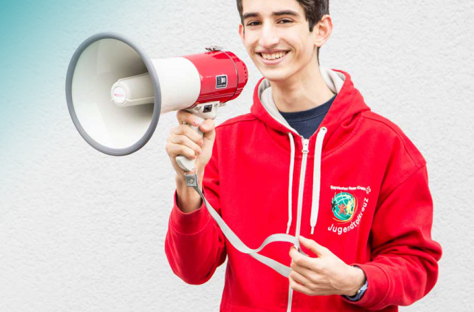 Ein Junge mit Megafon und rotem Kapuzenpulli auf dem das Logo des Jugendrotkreuzes prangt.
